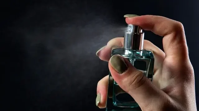 . A woman elegantly holds a spray bottle of perfume, preparing to apply it.