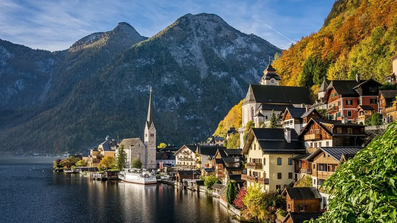 Scenic view of Hallstatt, Austria, showcasing vibrant autumn colors in the trees and reflections on the lake.