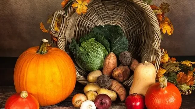 A basket filled with assorted vegetables and pumpkins rests on a rustic wooden table