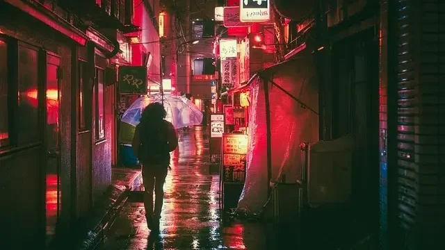 A woman walks through a dark alley at night, holding an umbrella to shield herself from the rain