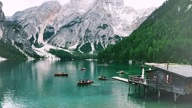 Canoes are docked on a serene lake beside a rustic cabin, surrounded by majestic mountains in the background.