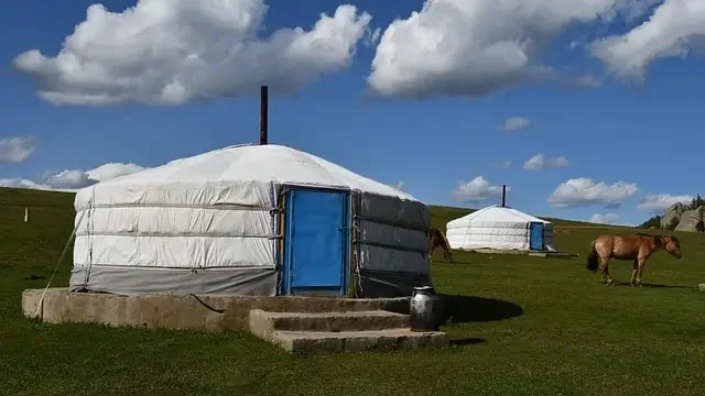 A yurt nestled in the mountains, surrounded by lush greenery and towering peaks under a clear blue sky