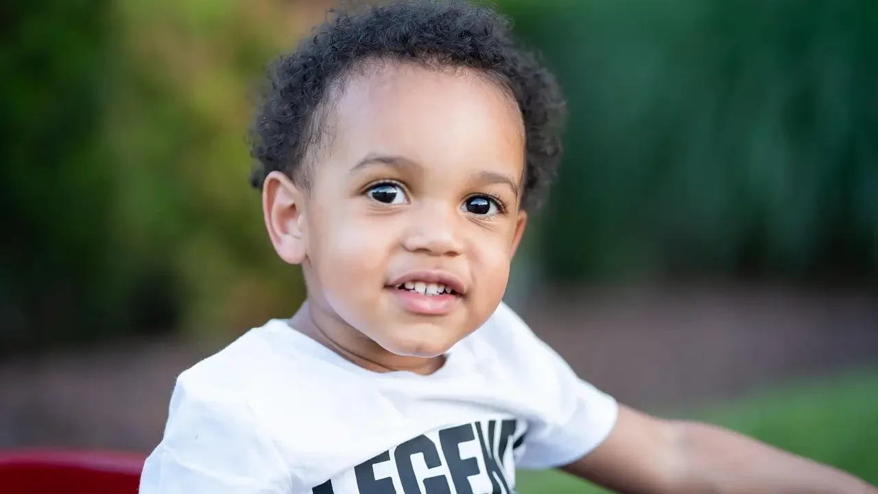 A young boy wearing a t-shirt with the word "Legend" printed on it, smiling and standing outdoors