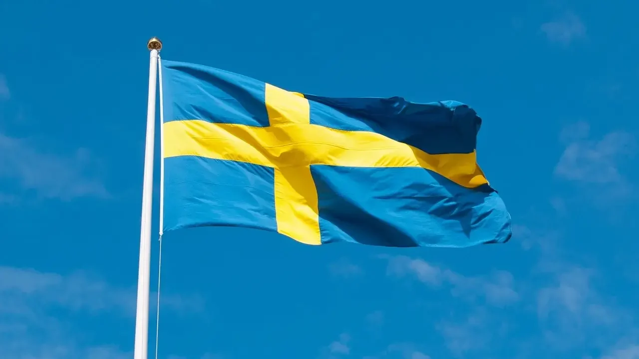 A Swedish flag waving in the wind against a clear blue sky