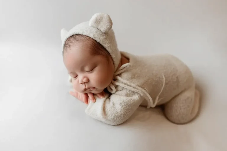Newborn baby dressed in a fluffy white bear outfit, peacefully sleeping on a soft blanket
