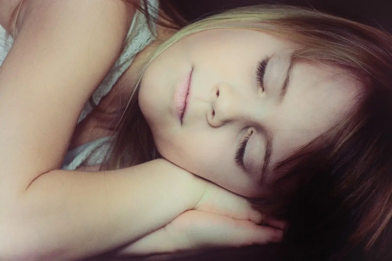 A young girl peacefully sleeping on a bed, surrounded by soft blankets and pillows