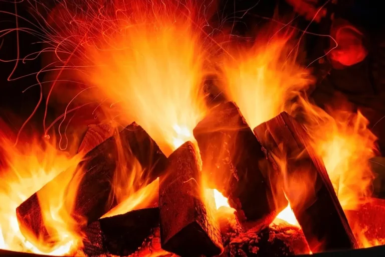 A metal bowl contains a vibrant fire, with bright flames dancing and illuminating the surrounding area.