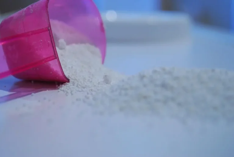 A pink plastic scoop filled with powder rests on a white table surface