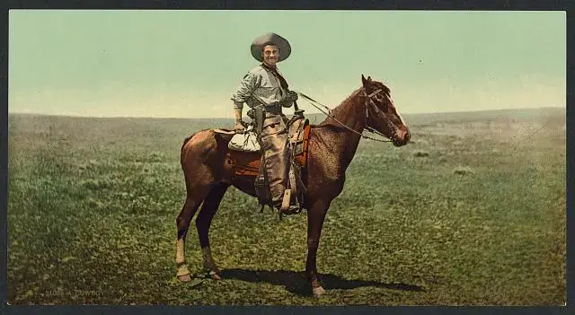 A cowboy riding a horse across a vast open field under a clear blue sky