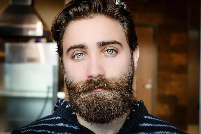 A man with a beard and blue eyes gazes thoughtfully into the distance