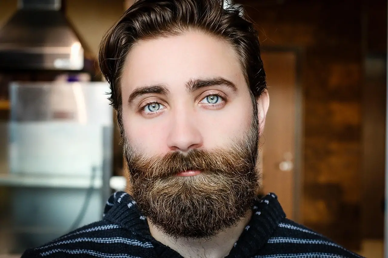 A man with a beard and blue eyes gazes thoughtfully into the distance