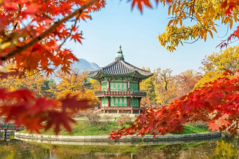 A serene pagoda nestled among vibrant autumn leaves in shades of red, orange, and yellow.