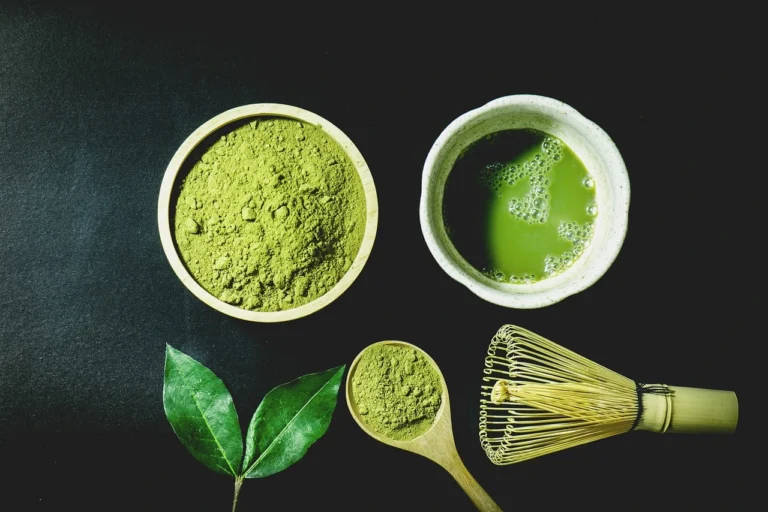 Matcha green tea powder and a bamboo whisk on a black background, highlighting the vibrant green color of the powder