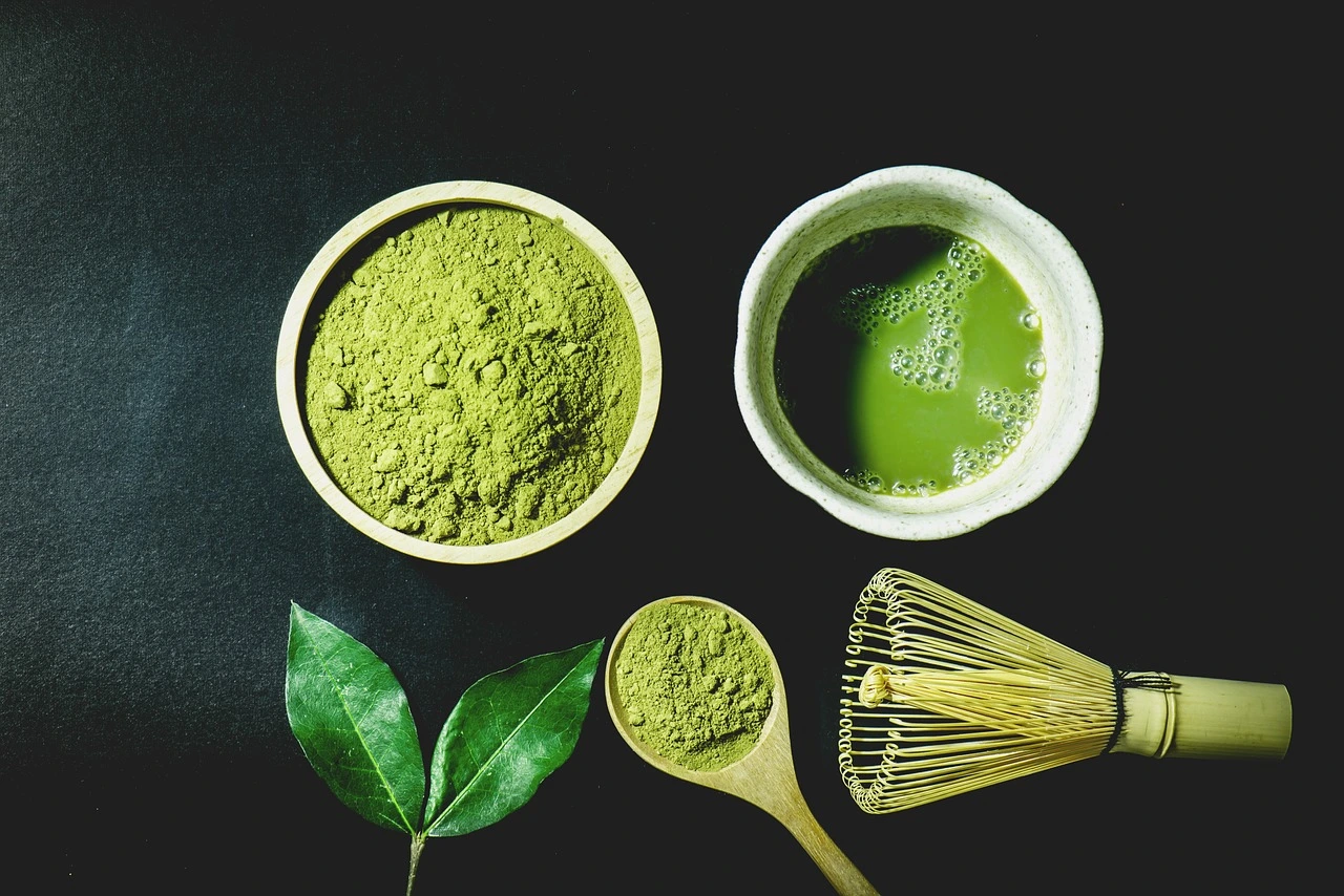 Matcha green tea powder and a bamboo whisk on a black background, highlighting the vibrant green color of the powder