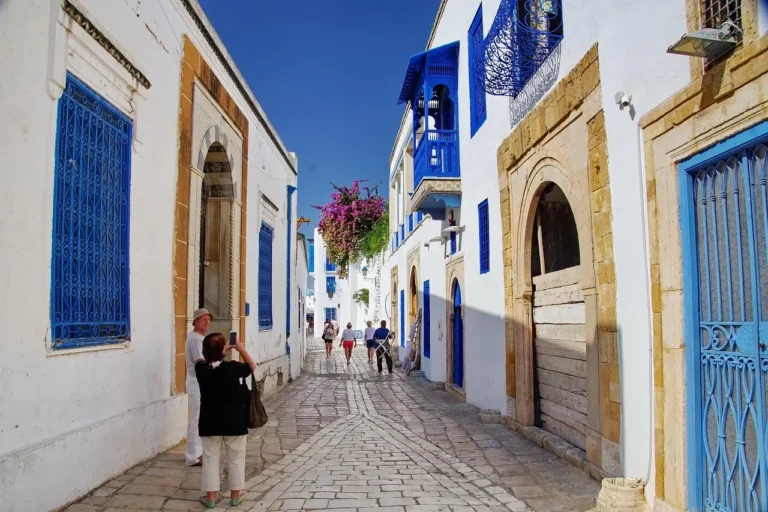 A narrow street lined with blue walls, featuring people walking and enjoying the vibrant atmosphere