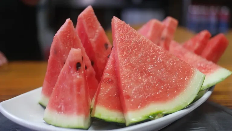 Fresh watermelon slices arranged neatly on a white plate, showcasing vibrant red flesh and green rind