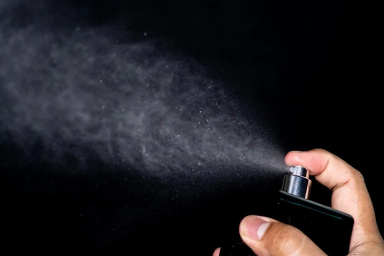 Perfume bottle spraying a fine mist showing why perfume may smell like alcohol at first.